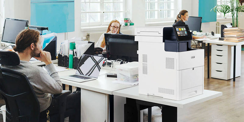 Two women collaborating in an office using a tablet next to a Xerox VersaLink C625 multifunction printer